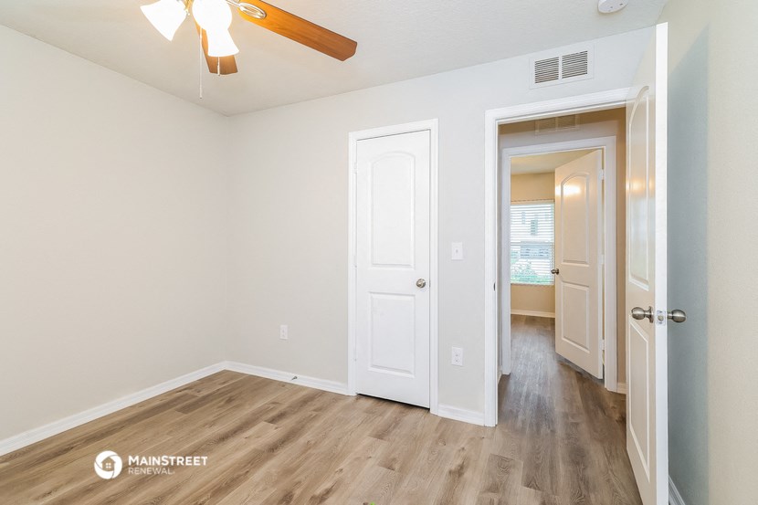 a living room with a door to a hallway and a ceiling fan