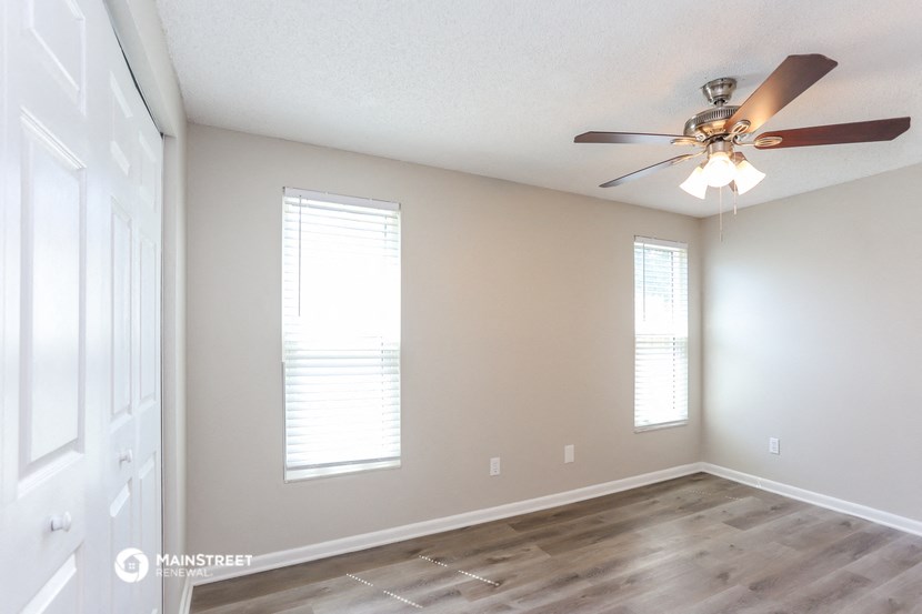 an empty living room with a ceiling fan and windows