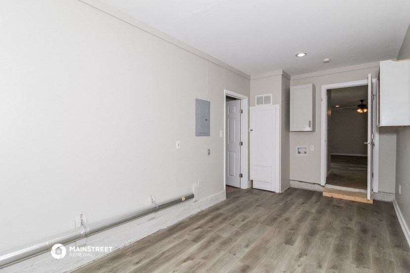 a living room with white walls and wood flooring and a door to a hallway