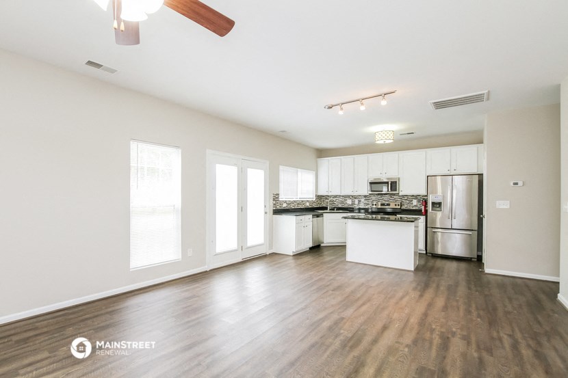 the living room and kitchen of an apartment with wood flooring and white cabinets