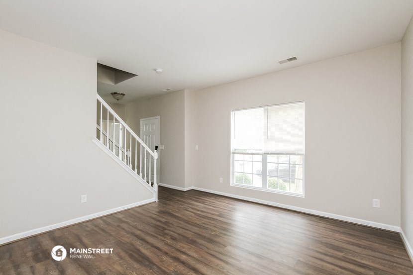 the living room of an apartment with wood flooring and a large window