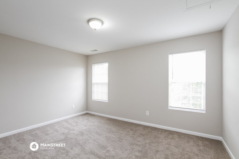 the spacious living room with two windows and carpeting