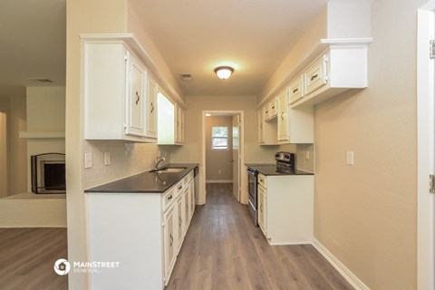 a kitchen with white cabinets and black counter tops and a door to a hallway