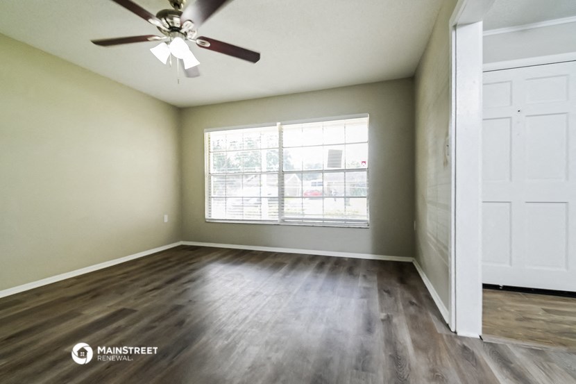 an empty living room with a window and a ceiling fan