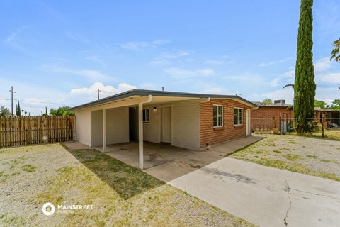 a small brick house with a driveway and a fenced in yard