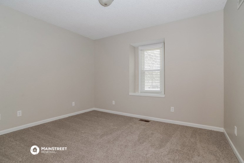 the spacious bedroom with carpeting and a window