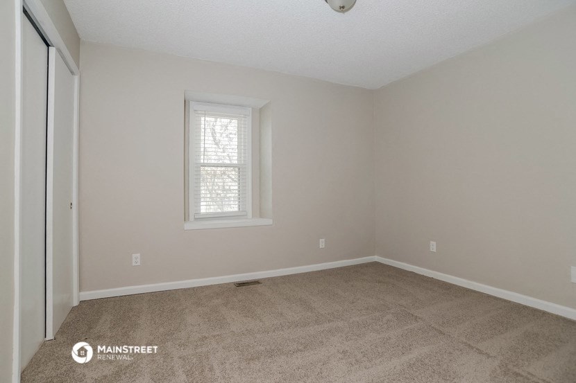 the living room of an empty home with carpet and a window