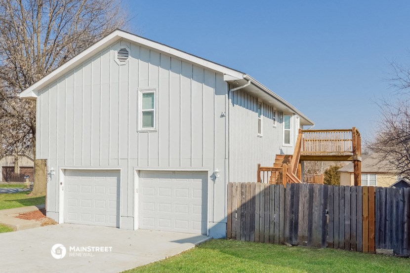 a white house with two garage doors and a wooden fence
