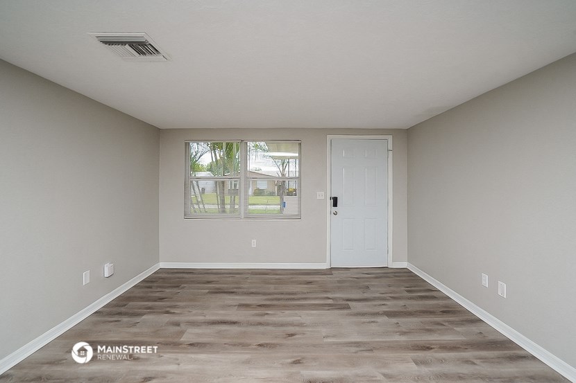 the spacious living room of an apartment with white walls and a white door