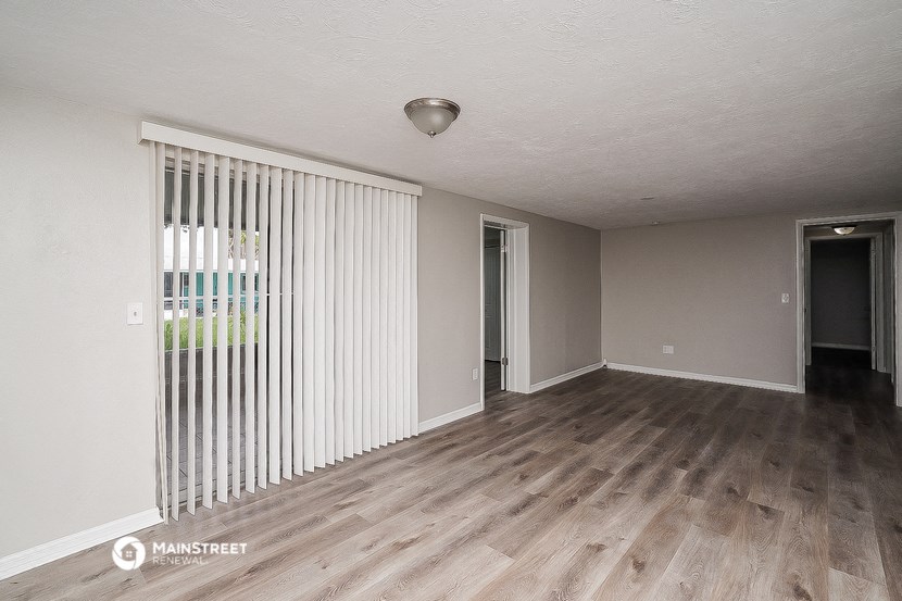 the living room and dining room of an apartment with wood flooring and a window