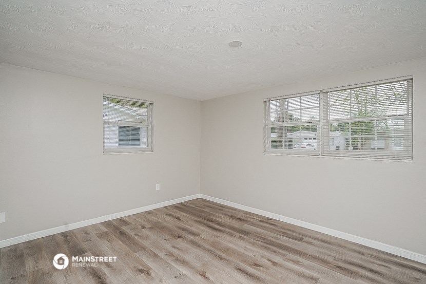 the living room of an empty home with wood flooring and two windows