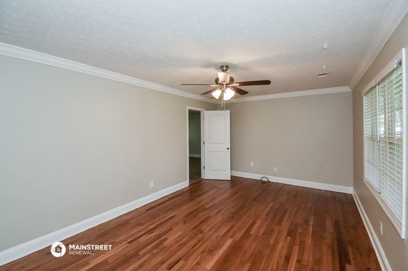 the spacious living room with hardwood flooring and a ceiling fan