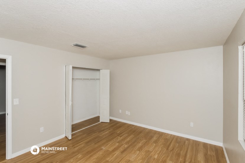 the spacious living room of an apartment with wood flooring and a closet
