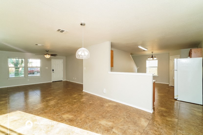 an empty living room with a kitchen and a refrigerator