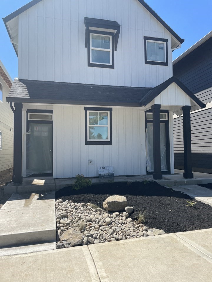 A white house with a black roof and a small garden in front.