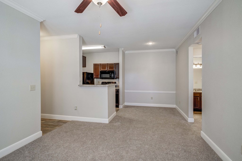 an empty living room with a kitchen and ceiling fan