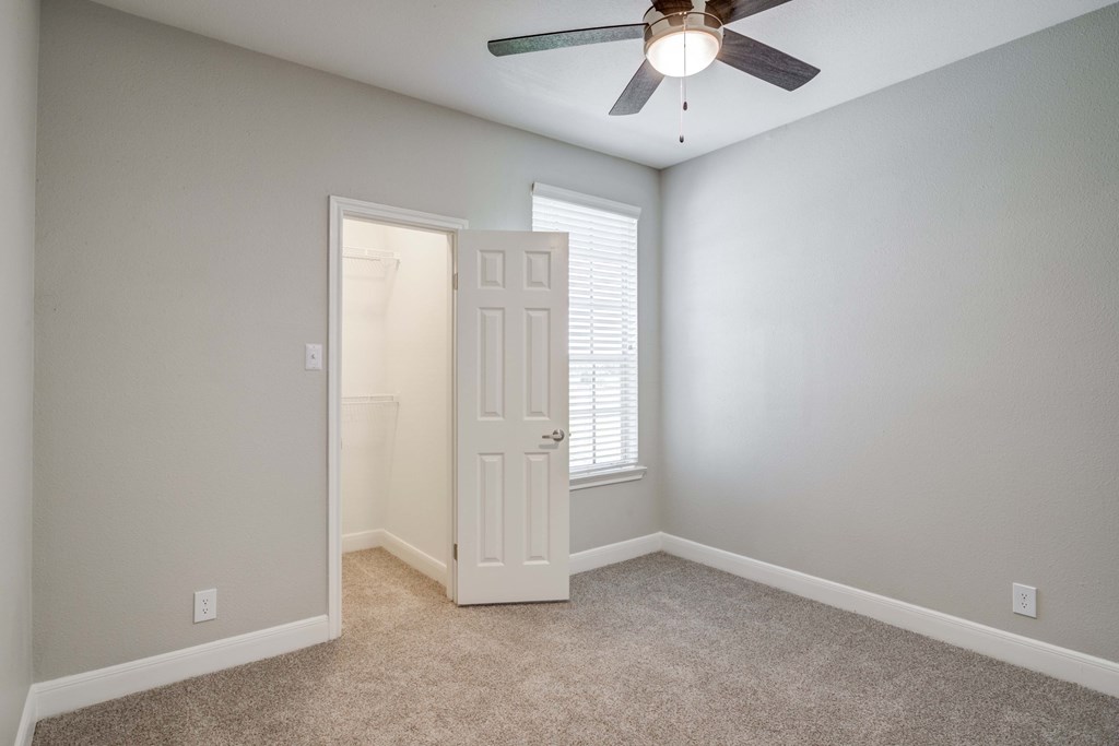an empty bedroom with a ceiling fan and a door to a closet