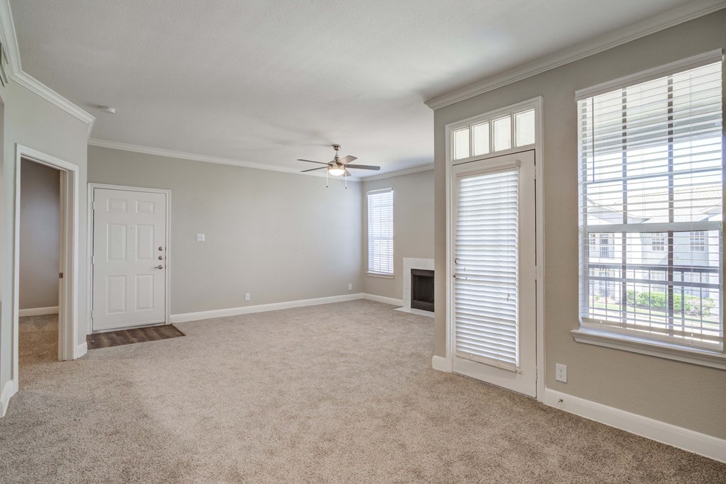 an empty living room with large windows and a ceiling fan