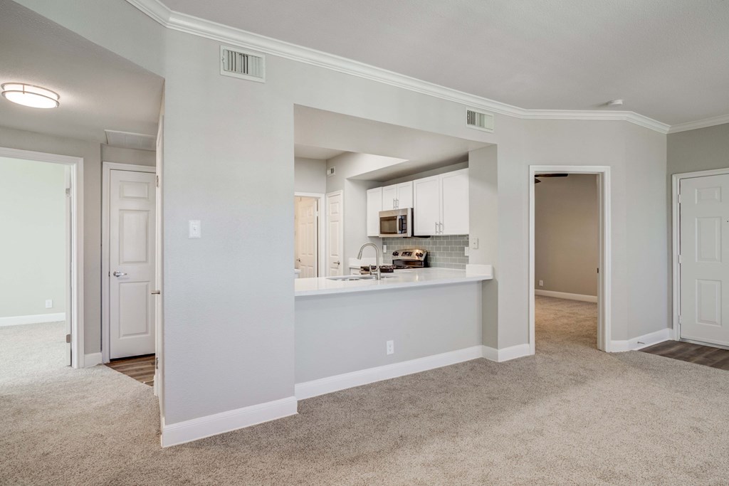 the living room and kitchen in a renovated home with carpeted flooring