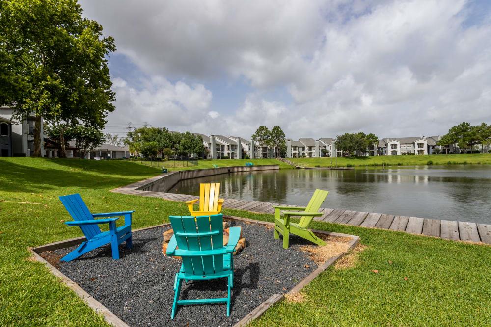 four colorful chairs sitting next to a lake with houses in the background