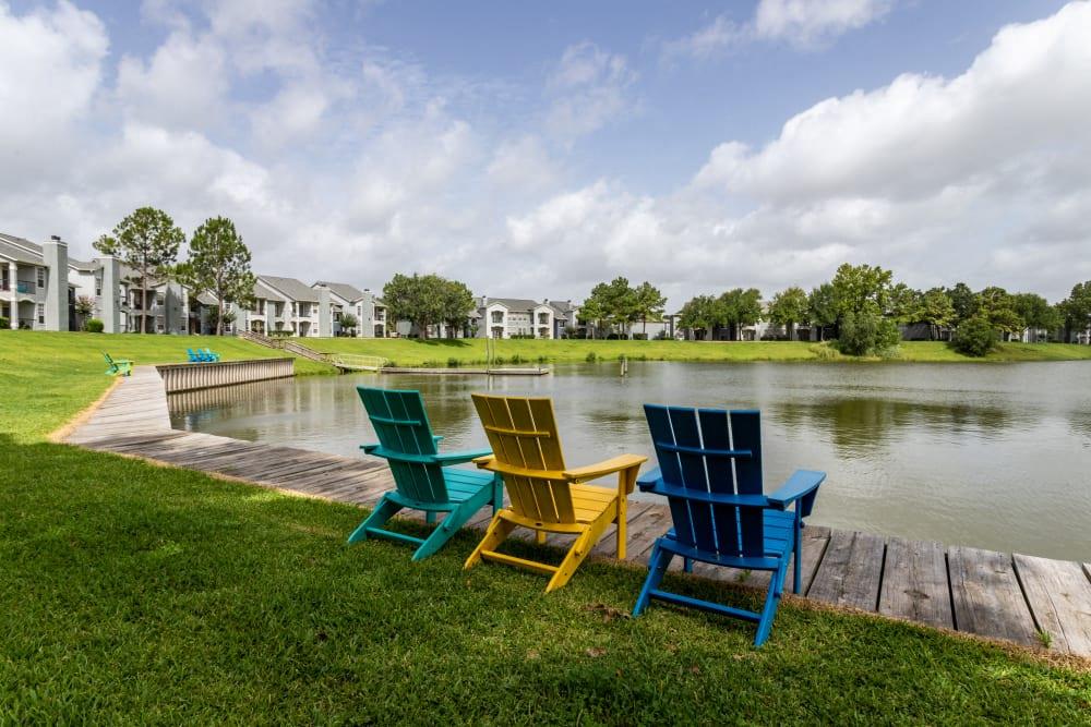 three colorful chairs sitting on a dock next to a lake