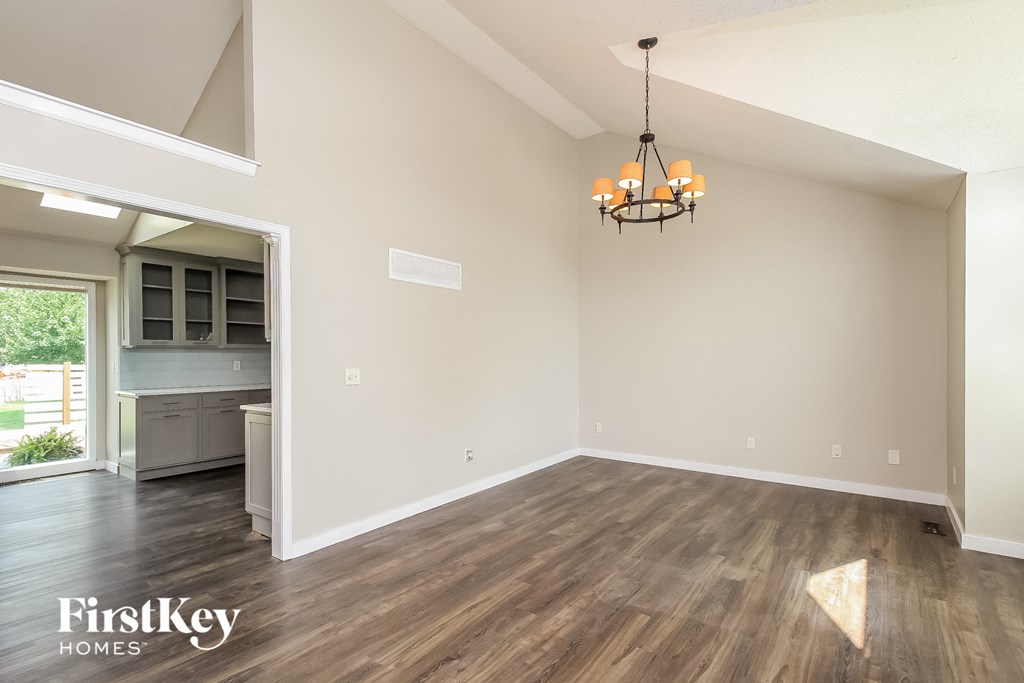 an empty living room with a chandelier and a kitchen