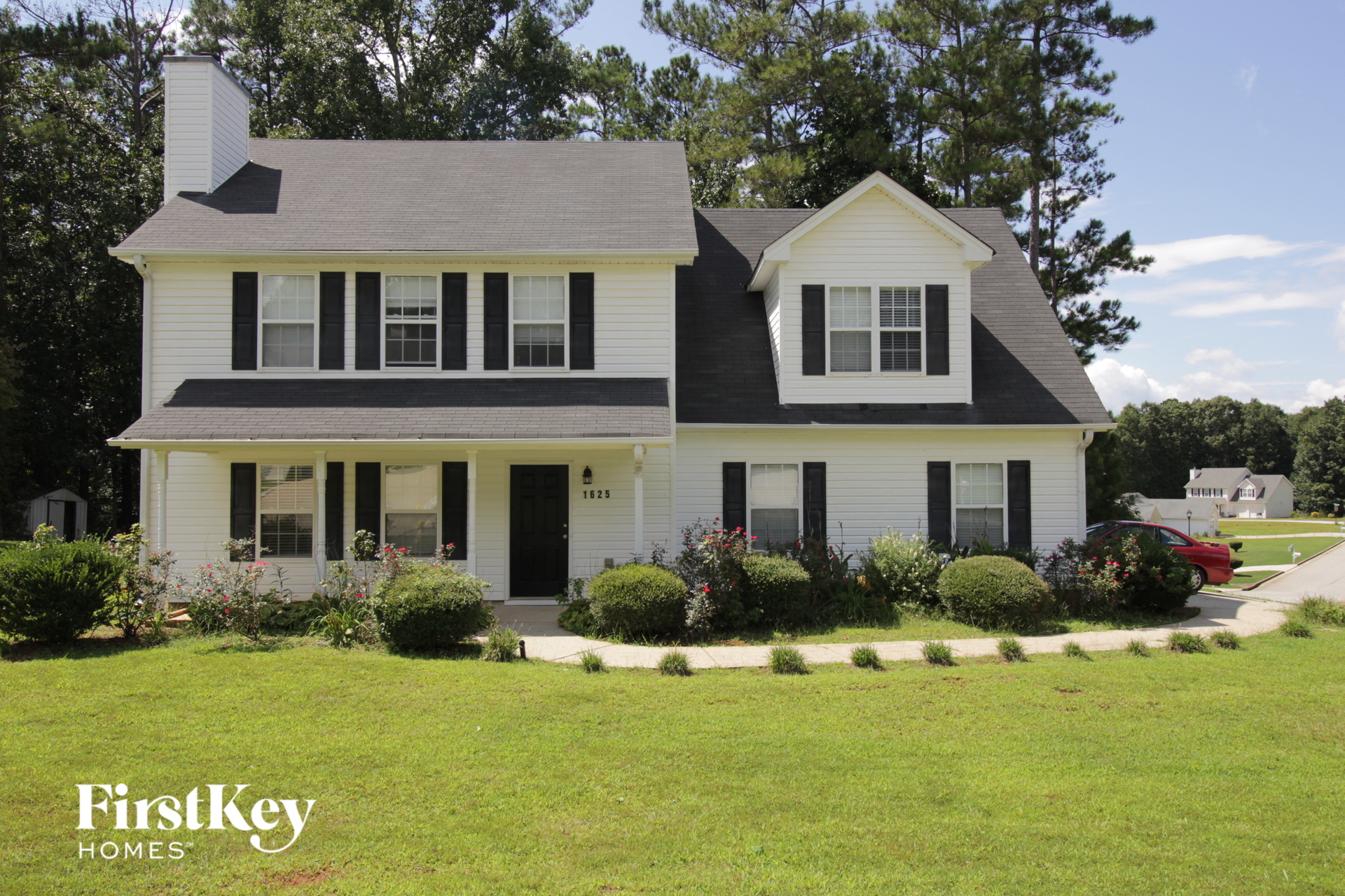 A white house with black shutters and a red car parked in front.