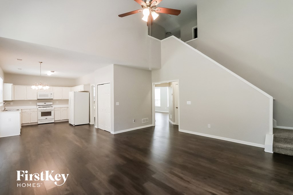 an empty living room with a ceiling fan and a kitchen