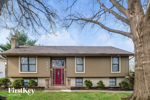 A beige house with a red door and a tree in front.
