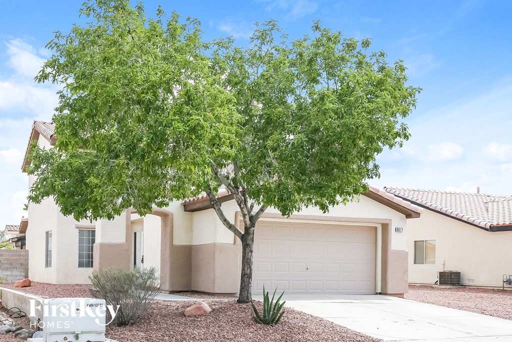 A tree in front of a house with a garage door.