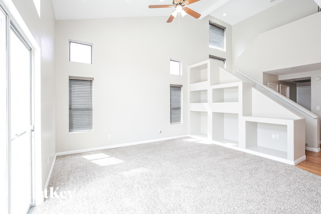 A spacious living room with a ceiling fan and built-in shelves.