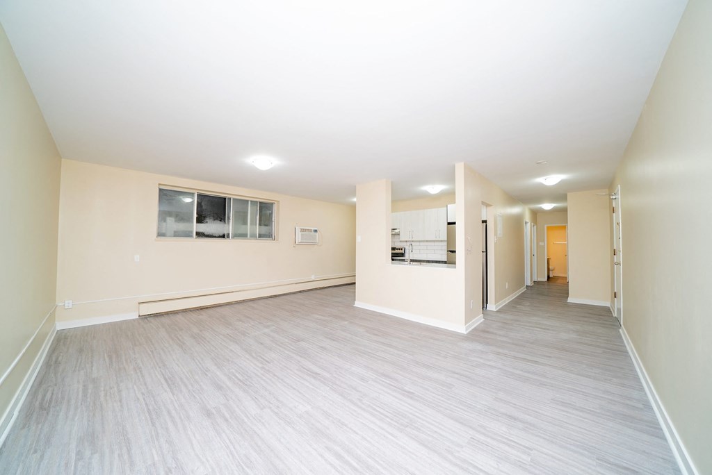 the living room and kitchen of an empty home with white walls and wood flooring