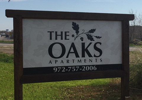 A sign for The Oaks Apartments with a phone number on it.