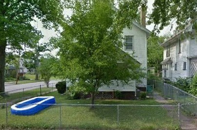 A blue inflatable pool is in a yard with a white house and a tree.