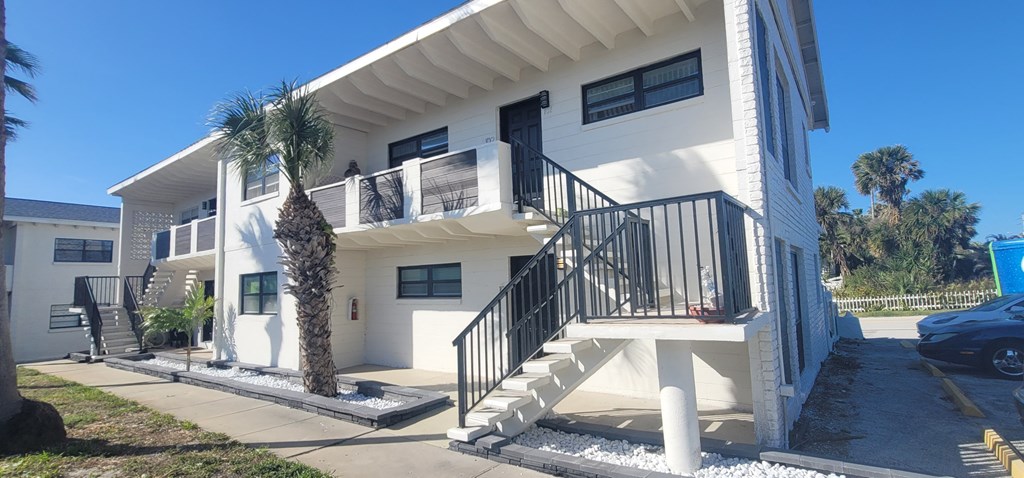 the exterior of a white house with stairs and palm trees