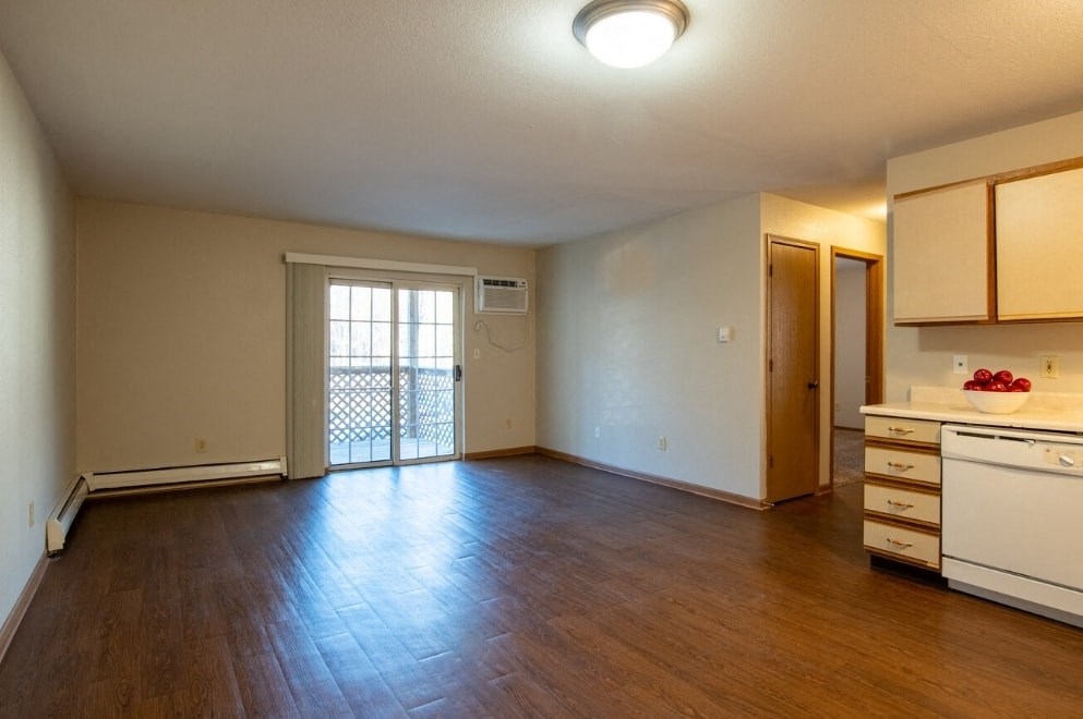 an empty living room and kitchen with wood flooring and a door to a balcony