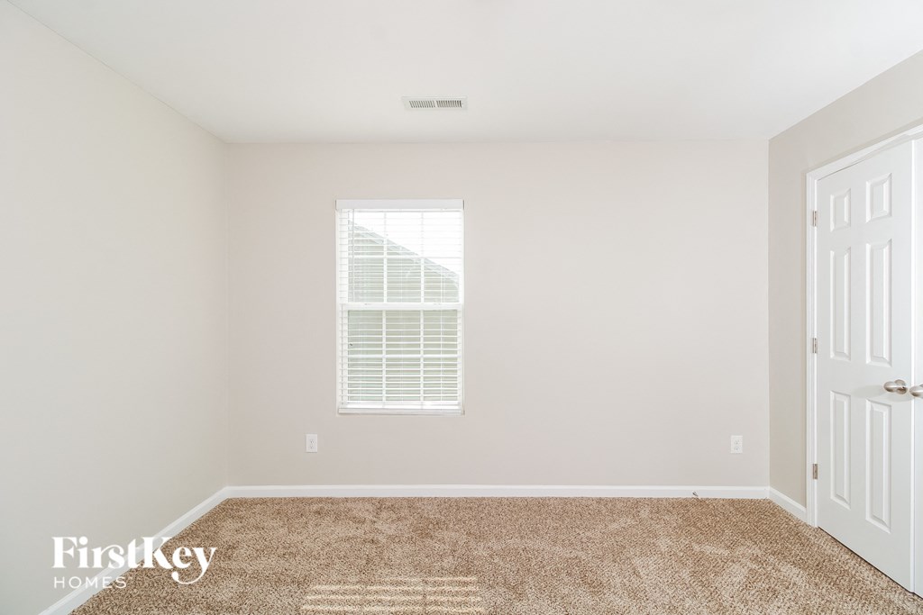 A room with a carpeted floor, a window with blinds, and a white door.