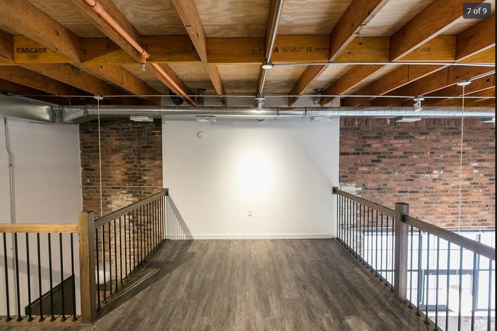 a loft with exposed brick and wood ceilings and a staircase