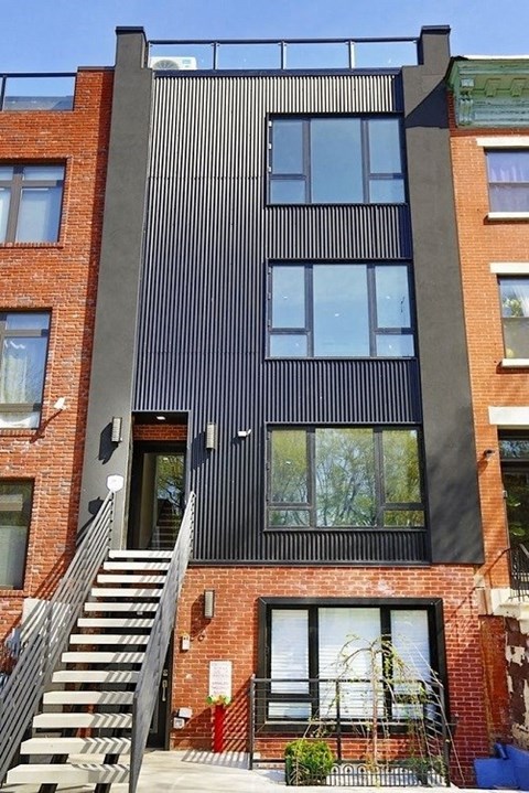 A modern house with a black facade and a staircase leading to the entrance.