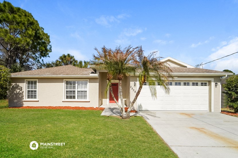 a white house with a palm tree in front of a driveway