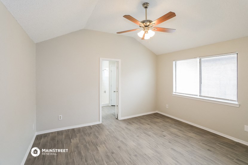 the spacious living room with wood flooring and a ceiling fan