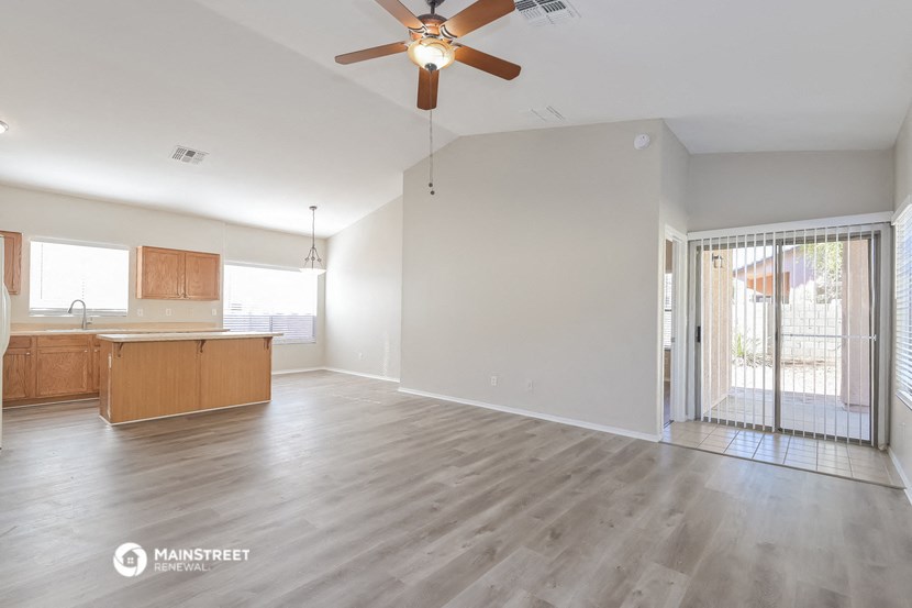 an empty living room with a kitchen and a ceiling fan
