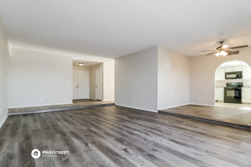 the living room of an apartment with wood flooring and a ceiling fan