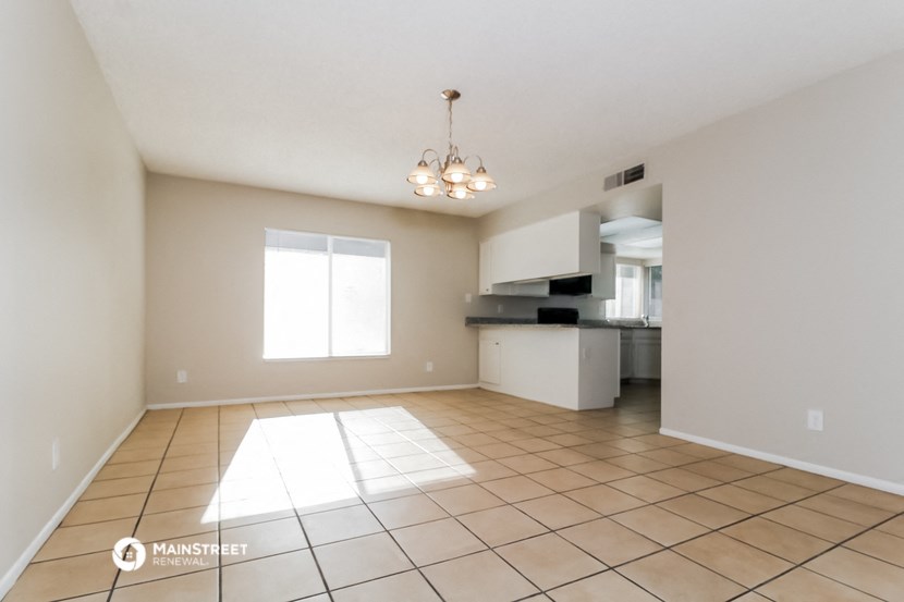 an empty living room with a kitchen in the background