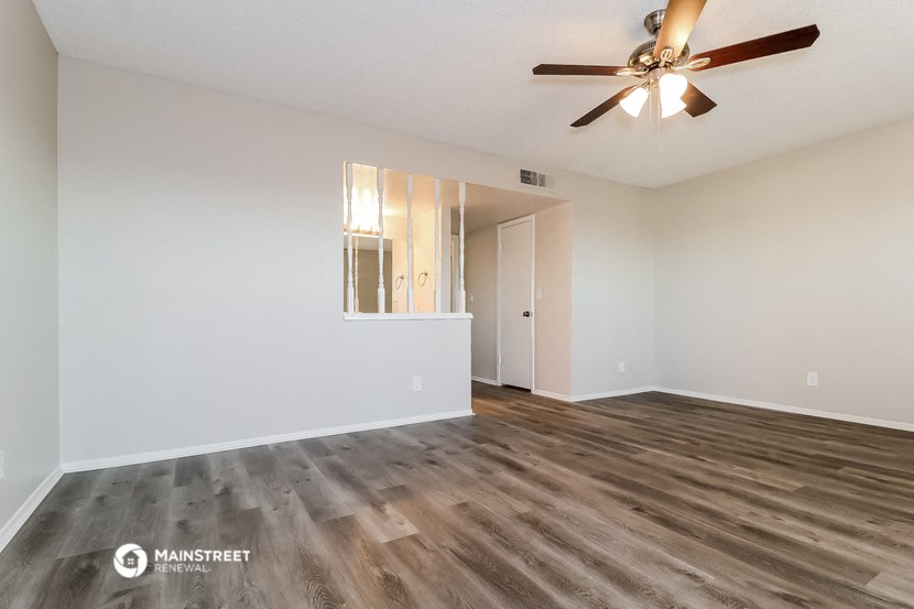 the spacious living room with hardwood flooring and a ceiling fan