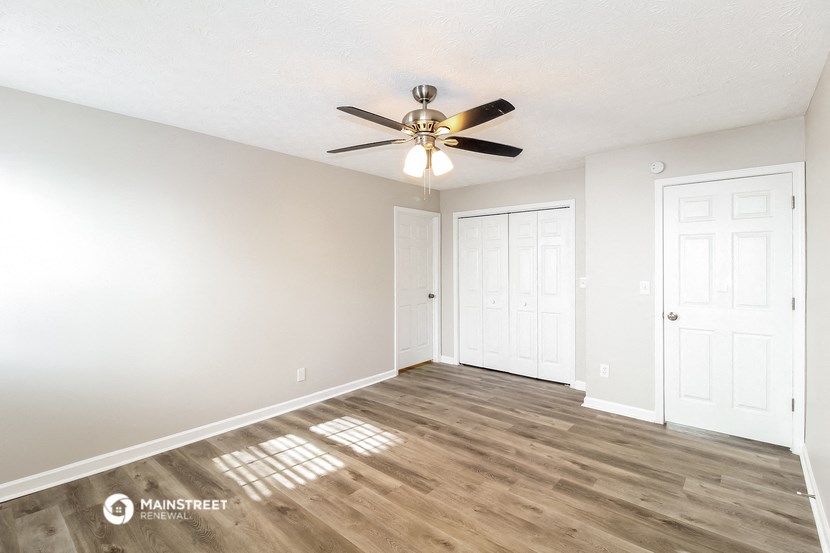 the spacious living room with a ceiling fan and white walls