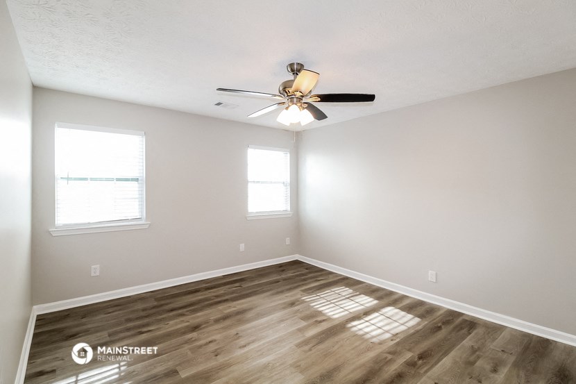 the spacious living room with wood flooring and a ceiling fan