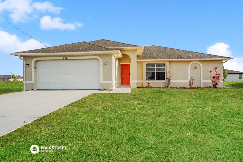 a beige house with a red door and a lawn