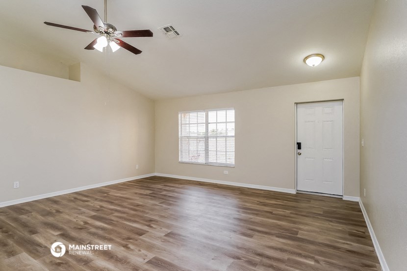 the spacious living room with hardwood flooring and a ceiling fan