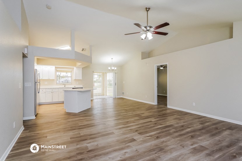 an empty living room with a ceiling fan and a kitchen